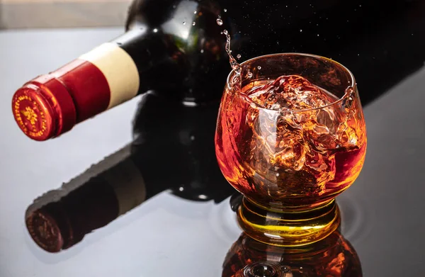 Botella de vino tinto con copa de vino. Salpicadura de agua y gotita en el reflejo negro . —  Fotos de Stock