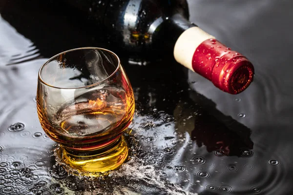 Бутылка красного вина с бокалом вина. Брызги воды и капли на черное отражение . — стоковое фото