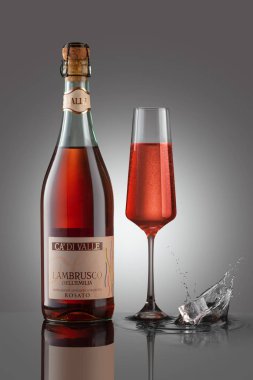 Gri arka planda şarap kadehiyle bir şişe köpüklü Lamrusco Rosato. Su sıçratan buz.. 