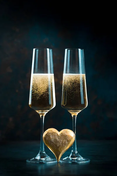 Zwei elegante romantische Gläser mit goldglitzerndem Champagner mit goldenem Herz vor dunkelblauem Hintergrund. Valentinstag. — Stockfoto