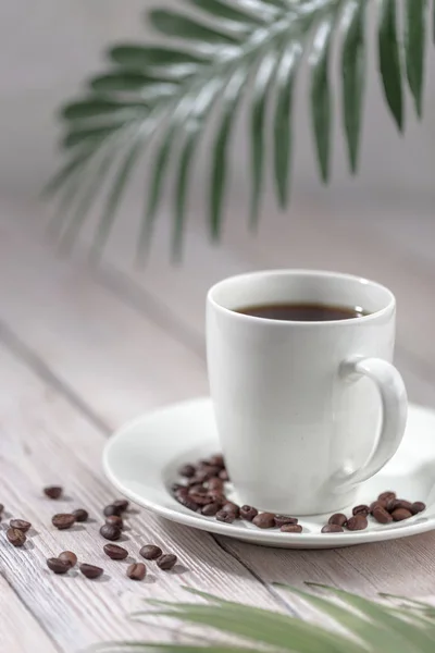 Cierre una taza de café caliente con granos de café tostados en la mesa de madera blanca . — Foto de Stock