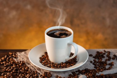 Beyaz kahve fincanı ve ahşap arka planda kahve çekirdekleri.