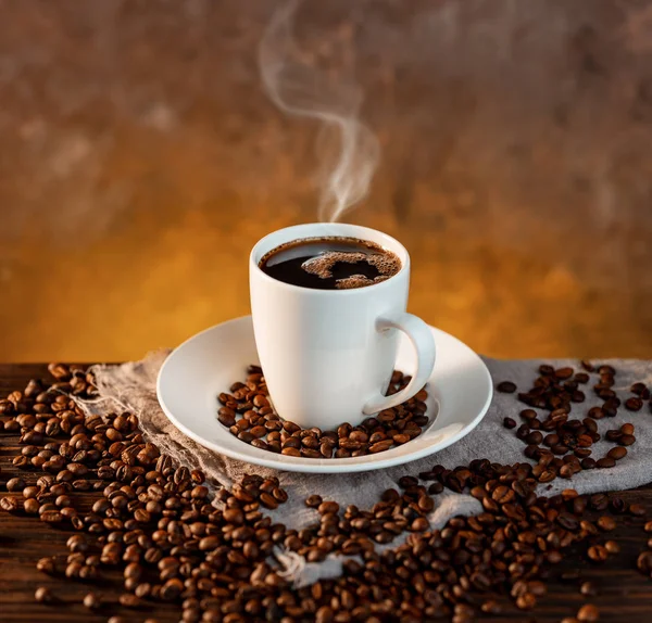 Beyaz kahve fincanı ve ahşap arka planda kahve çekirdekleri. — Stok fotoğraf