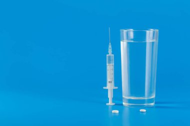 Su dolu cam ve mavi arkaplanda izole edilmiş çeşitli haplar.