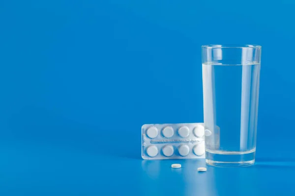 Glass with water and various pills isolated on blue background with copy space — 스톡 사진