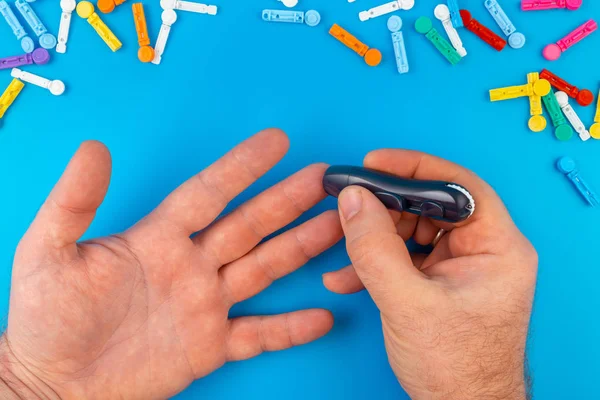 Diyabet testi. Adamın elleri mavi arka planda kan şekeri seviyesini Glikoz sayacına göre kontrol ediyor. Kan şekeri seviyelerini ölçen bir cihaz. Test bantları, mavi arka planda haplar.. — Stok fotoğraf