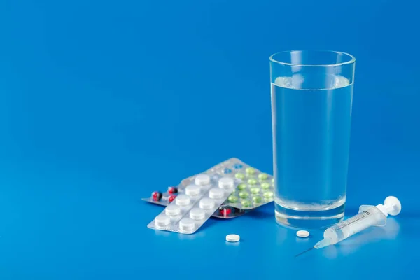 Glass with water, pills, syringe on blue background with copy space — 스톡 사진