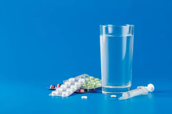 Üveg vízzel, tabletták, fecskendő kék háttér másolási hely — Stock Fotó