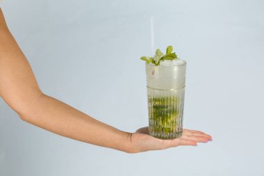 Turuncu arka planda bir bardak tropikal mojito kokteyli tutan bir adamın eline yakın çekim. Yaz tatili konsepti.