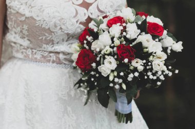 Gelinin elinde güllerle taze bir buket ve gelinliğin önünde kurdeleli yaprakların olduğu kısmi manzara