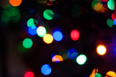 Duvar kağıdı ve tasarım için bokeh etkisi ile siyah bulanık arkaplan üzerine odaklanmış çok renkli geleneksel Noel ışıkları