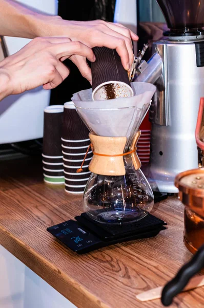 cropped view of barista pouring ground coffee with paper cup in glass flask on electronic balance on wooden table in caffe