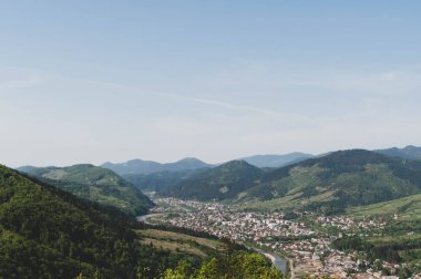 Nehir kıyısındaki şehrin üst manzarası. Mavi gökyüzünün altında. Yeşil ormanlı büyük dağların arasında.