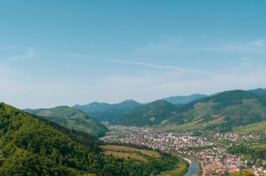 Vadideki ve mavi gökyüzünün altındaki nehir manzarası yüksek dağların arasında yeşil odunlarla kaplı.