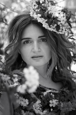 Uzun saçlı güzel bir kadının beyaz ve siyah portresinin yumuşak odağı bahçedeki çiçek açan kiraz dallarının yanındaki kameraya bakıyor.