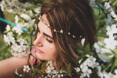Çiçekli uzun saçlı güzel bir kadının portresinin yumuşak odağı. Etrafı beyaz çiçeklerle dolu kiraz dallarıyla çevrili.