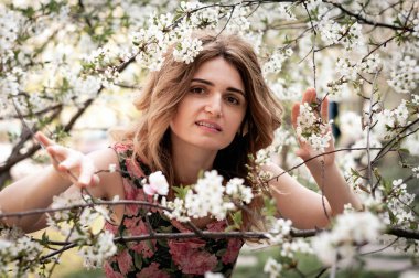Ağaç dallarından geçen ve güneşli bahçedeki kameraya bakan çiçek açan güzel, gülümseyen bir kadının yumuşak odağı.