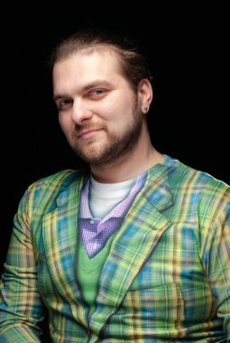 Yakışıklı, pozitif sakallı bir adamın portresi. Şık giyinmiş, yeşil bir küpe takmış. Siyah üzerine izole edilmiş kameraya bakıyor.