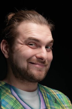 Yakışıklı, sakallı, şık saçlı, suratını buruşturan ve siyah kameraya bakan bir adam.