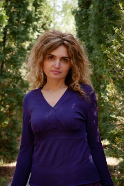 Yeşil thuja 'nın önünde uzun saçlı ve bahçedeki kameraya bakan güzel, kendine güvenen bir kadının yumuşak odağı.