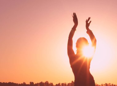 Sıska bir kadının karanlık, parıldayan silueti elleri havada güneş ışığıyla aydınlanmış gündoğumunda Aurora gökyüzünün önünde geleneksel kabile göbeğiyle dans ediyor.