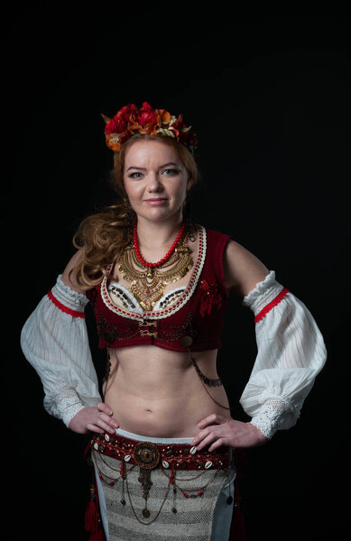 attractive confident dancer in traditional folk slavic costume holding hands on hips and looking at camera on black background