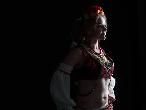 low-key portrait with back light of woman in traditional folk ukranian costume holding hands on hip and looking away isolated on black