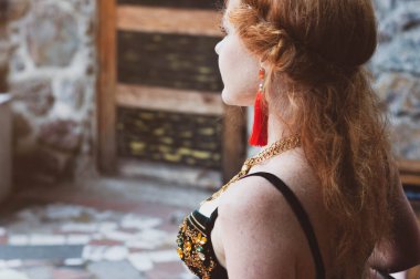 Uzun saçlı, kırmızı küpeli, yeşil kostümlü dansçının yan görünüşü