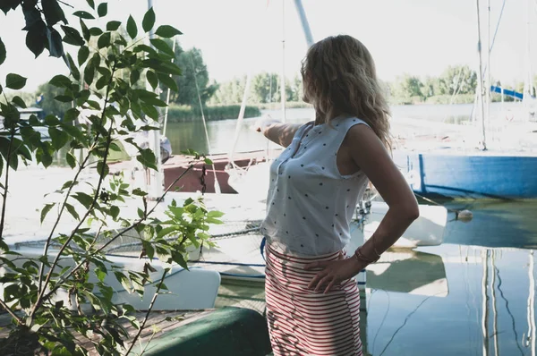 Side View Of Woman In White Blouse And Red Skirt Gesturing With Outstretched Hand At Boats On River Copy Space Sunlight Stock Photo