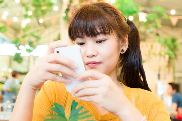 Portrait of asian beautiful nerd girl using mobile smart phone in cafe blurred background.
