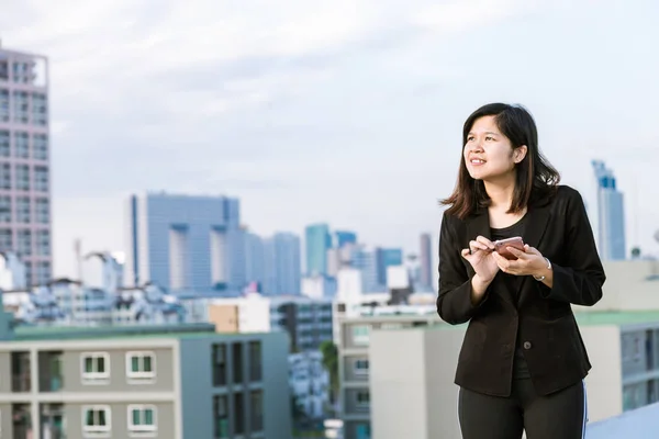Happy Asian Businesswoman talking on smart phone with building background.
