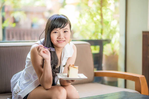 ケーキが付いているソファーの上に座って美しい笑みを浮かべてアジア若い女性 — ストック写真