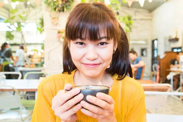 ラテ黒マグカップを保持しているアート コーヒー ショップに座っているアジア女性を笑顔 — ストック写真
