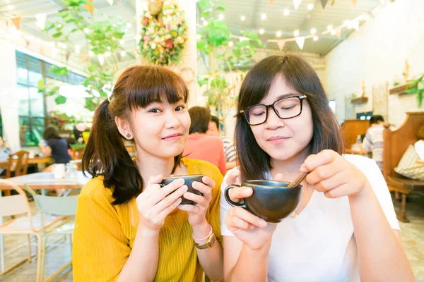 Smiling female asian friends holding coffee mugs while talking b