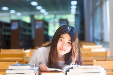 Mutlu öğrenci kadın sittng okumak için penceresinden ışık ahşap sandalye üzerinde kütüphane kitapları