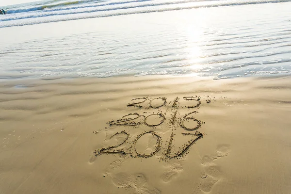 New year 2017 written on seashore sand at sunrise with wave