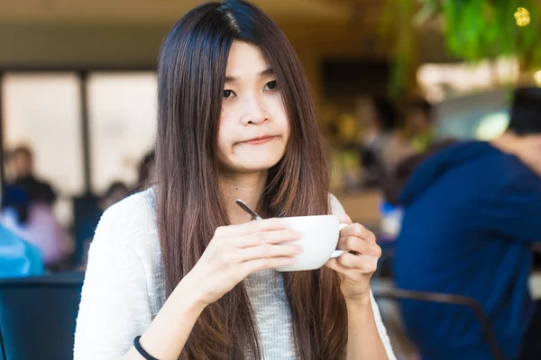 学生妇女拿着一杯拿铁咖啡在她的手在图书馆背景 而思考业务 — 图库照片