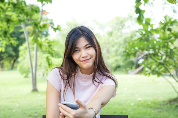 緑豊かな公園のベンチに座っているクローズ アップの一方で スマート フォンを使用して魅力的な少女 — ストック写真