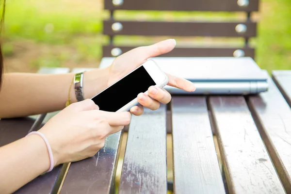 Chica atractiva joven usando el teléfono inteligente mientras está sentado en un banco — Foto de Stock