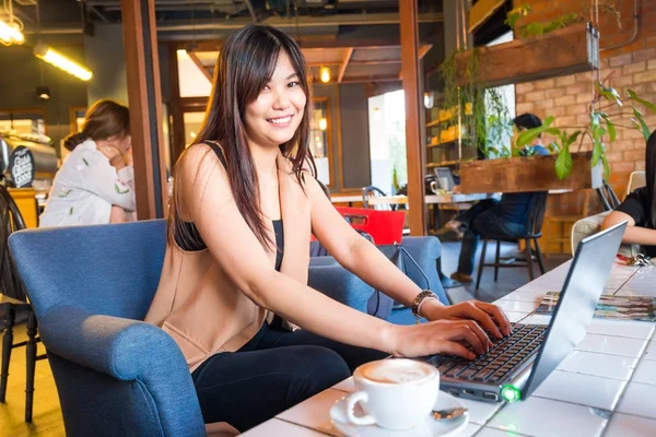 Mujer joven asiática independiente sentada en la cafetería con portátil — Foto de Stock