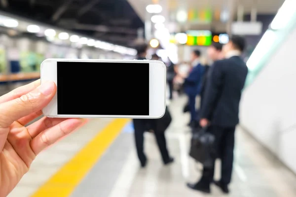 Pantalla en blanco del smartphone en mano en la estación de tren — Foto de Stock