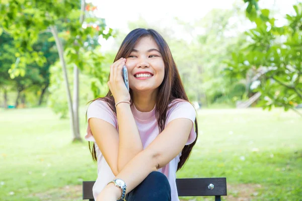 Donna seduta sulla panchina con smartphone nel parco cittadino . — Foto Stock