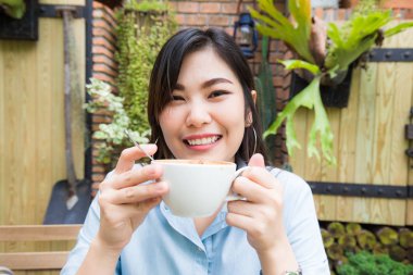 Asyalı kadınlar beyaz latte sanat kahve Kupası ile kafe Bahçe arka plan kadınlarda rahatla.