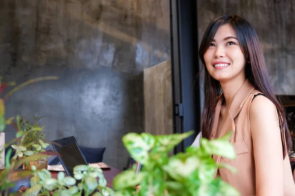 Gülümseyen serbest genç Asyalı kadın online çalışma için laptop ile kafeteryada oturan