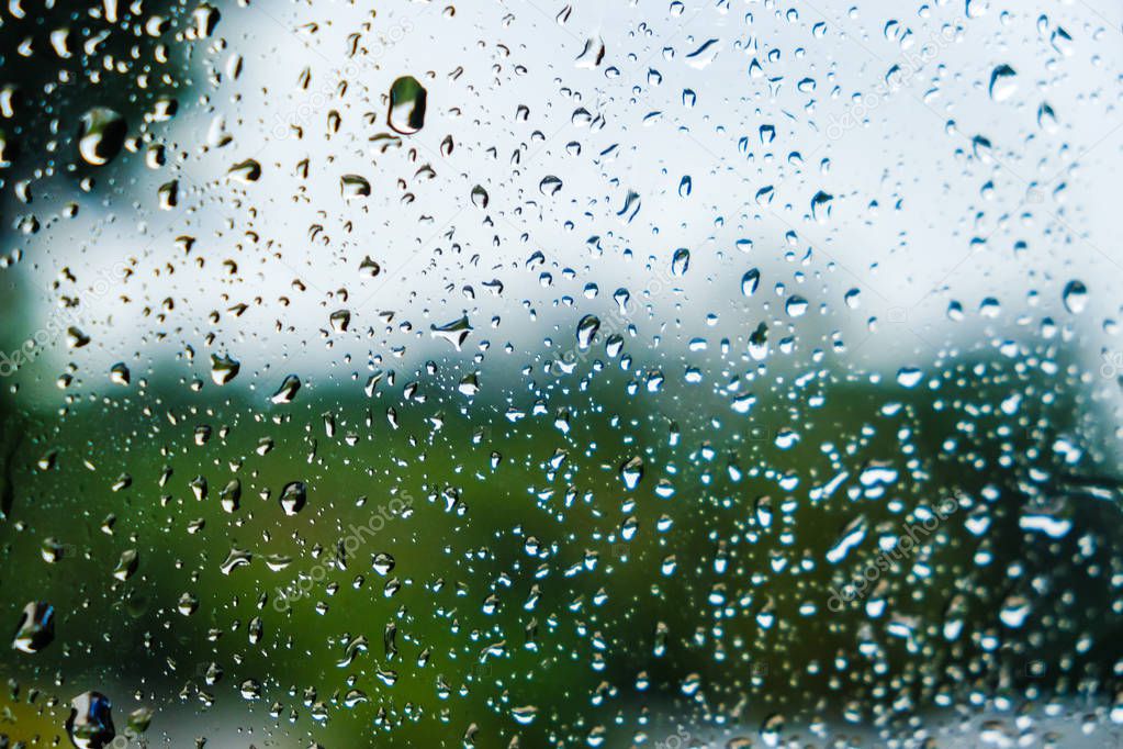 Drops of rain on window with blurred green nature 