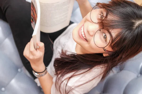 여자 착용 안경 아늑한 소파에서 책을 읽고 — 스톡 사진