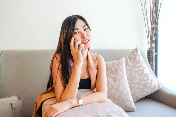 Bella giovane donna asiatica che parla con il telefono cellulare sul divano — Foto Stock
