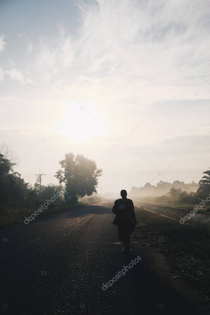 Buddha monk walking dhutanga for food donation in the morning sunrise on rural road