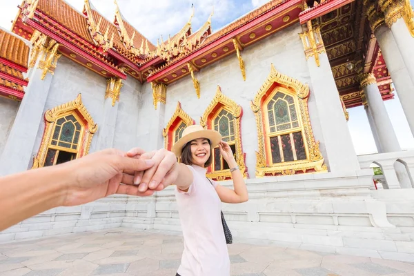 Asian tourist women in hat leading man hand to travel at marble temple, Thailand