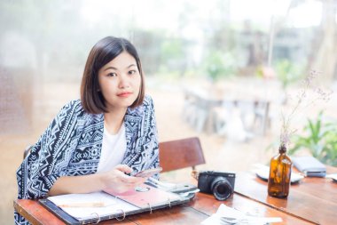 Asyalı genç kadın kahve dükkanı ahşap masa içinde otururken cep telefonu kullanmak